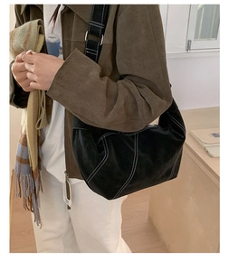 Detail of black suede hobo bag featuring white contrast stitching and adjustable strap