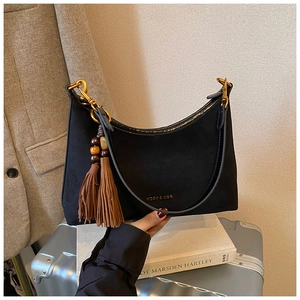 Detail of black suede shoulder bag with gold logo and brown double tassel charm