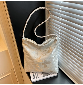 Detail of light blue satin bag with golden butterfly pattern and woven rope strap