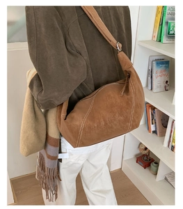 Close-up of brown suede hobo bag with white stitching and stylish wide shoulder strap
