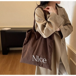 Detail of dark brown corduroy tote bag with white Nice letter print on model shoulder