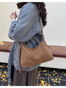 Brown suede hobo shoulder bag worn with a gray wool coat over autumn ginkgo leaves