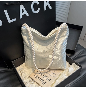 Detail view of the silver glitter tote bag with woven handles inside a black gift box