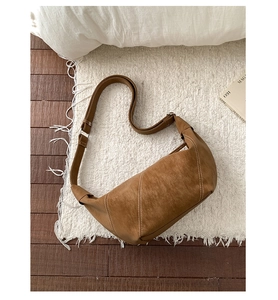 Detail of brown suede crescent bag featuring contrast white stitching and wide strap