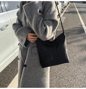 Detail of black rhinestone shoulder bag with twisted strap on grey wool coat