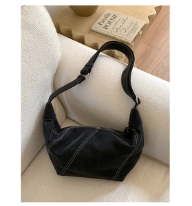 Close-up of black suede hobo bag with contrast white stitching on a cozy sofa