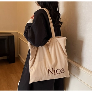 Detail shot of beige corduroy tote bag showing 'Nice' embroidery and striped texture