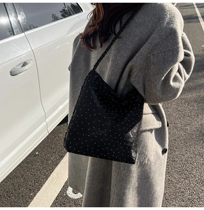 Detail of black tote bag with white polka dots and woven rope straps worn with a coat