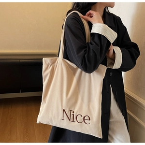 Detail of cream corduroy tote bag showing textured fabric and brown Nice embroidery