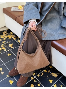 Close-up of brown suede shoulder bag in an autumn outdoor setting with ginkgo leaves