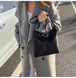 Detail of black rhinestone shoulder bag with woven handle on grey coat street style
