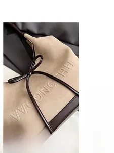 Close-up of contrast suede tote bag with embossed lettering and bow detail