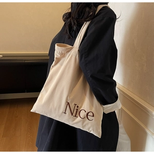Detail of off-white corduroy tote bag with Nice embroidery shown on model shoulder
