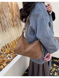 Detail of dark brown suede shoulder bag with adjustable strap in an autumn setting