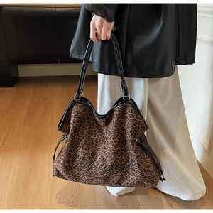 Detail of leopard print tote bag featuring black leather handles and embroidered text