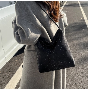 Close-up of black tote bag with white polka dots and woven strap in street setting