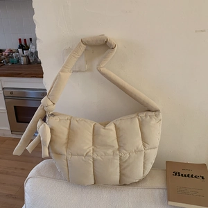 Détail d'un sac matelassé crème avec nœud décoratif et bandoulière rembourrée moelleuse