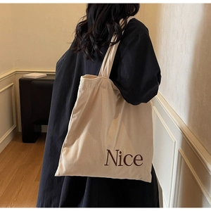 Detail view of beige corduroy tote bag with Nice embroidery on a model back