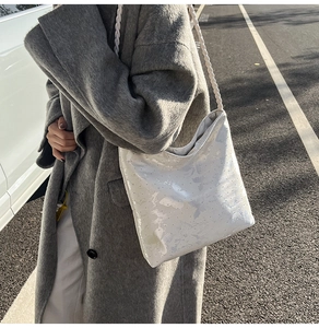 Detail of white patent leather shoulder bag with woven strap on grey wool coat