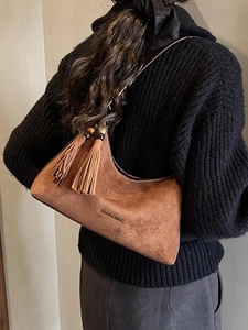 Brown suede hobo bag with tassel detail and embossed logo shown on model's shoulder