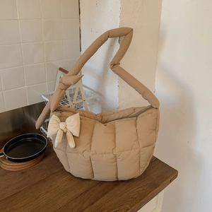 Gros plan d'un sac à bandoulière matelassé beige avec texture douce et détail de nœud charm