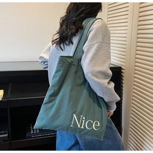 Detail of dark green corduroy tote bag featuring white Nice embroidery and vertical texture