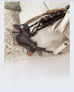 Détail d'un porte-clés teckel en cuir marron accroché à un sac à dos en cuir blanc cassé