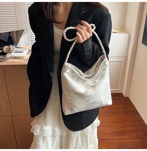 Detail of white satin shoulder bag with floral embroidery and woven rope handle