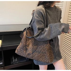 Detail of leopard print tote bag with black embroidery and leather handles on model
