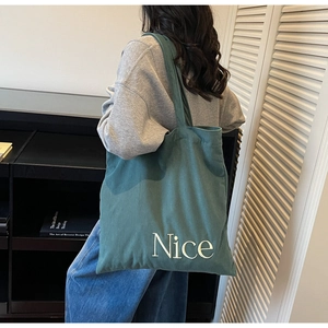 Detail of green corduroy tote bag with Nice embroidery shown on model in a cozy setting