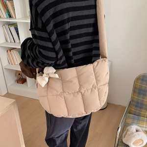 Détail de la sacoche matelassée beige avec un pendentif nœud en tissu blanc sur la sangle