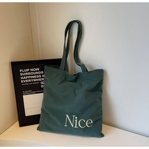 Detail shot of green corduroy tote bag with Nice lettering on a white surface