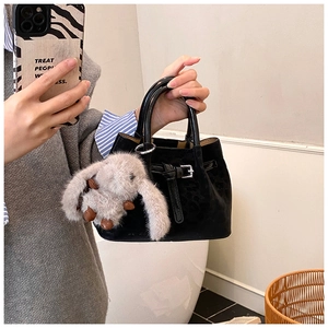 Close-up of black suede bucket bag with a cute plush rabbit charm and buckle detail
