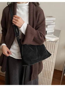 Detail of black suede tote bag with white stitching and adjustable strap on a model