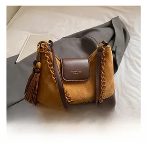 Detail of retro suede crossbody bag with gold chain strap and elegant leather tassel charm