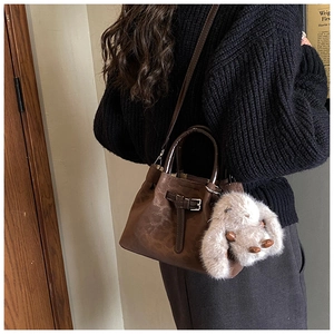 Detail view of retro brown leather bucket bag with cute plush bunny charm on a model