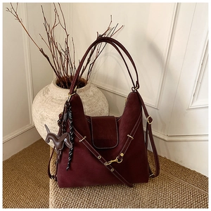 Detail of burgundy suede shoulder bag with woven strap and puppy-shaped leather charm