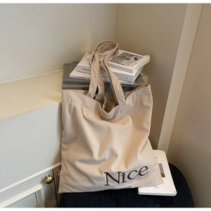 Detailed view of beige corduroy tote bag featuring brown Nice letter embroidery and texture