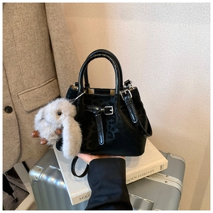 Close-up of black leather bucket bag with metallic buckle and white plush bunny charm