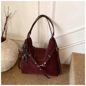 Detail of burgundy suede shoulder bag with gold buckle and leather dog charm decoration