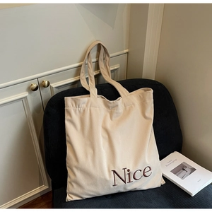 Detail of cream corduroy tote bag featuring brown Nice embroidery and ribbed texture