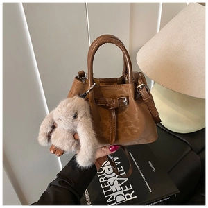 Brown leather bucket bag detail with adjustable buckle strap and plush rabbit charm