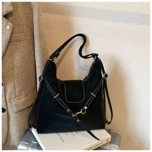 Close-up of black hobo bag with white stitching on travel luggage and books