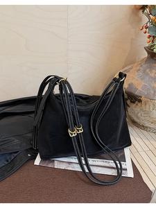 Detail of black leather hobo bag with white contrast stitching and gold metal hardware