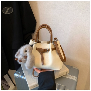 Detail view of the beige bucket bag with a brown handle and a cute grey rabbit charm