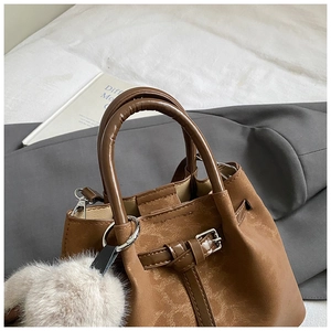 Close-up of a vintage brown bucket bag with dual handles and a fluffy plush pompom charm
