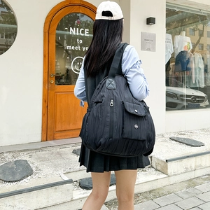 Close-up of black pleated nylon backpack showing functional pockets and metal buckle detail