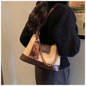 Détail du sac en daim matelassé avec chaîne dorée et pompon porté par le mannequin