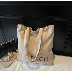 Close-up of off-white corduroy tote bag with Nice lettering and minimalist office accessories