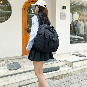 Outdoor street view of a black pleated nylon backpack with double handles and a metal logo